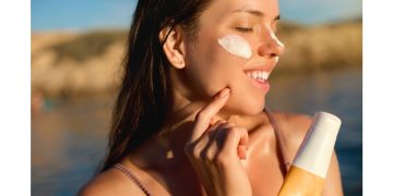 uśmiechnięta kobieta nakładająca krem do opalania na plażę